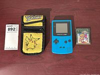 Photo showing all items in lot: Blue Game Boy Color, Wario Land 3 cartridge, and yellow Pokémon carrying case with Pikachu.