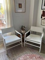 Two CB2 white leather safari arm chairs side by side in a room