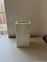 Rectangular white marble vase with honed finish placed on a flat surface against a neutral wall, showing marble veining and thickness.