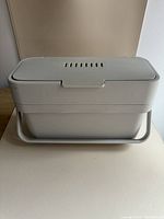 Joseph Joseph compost bin showing front and overall shape, gray color, with carrying handle at the base