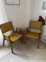Two wooden framed armchairs with mustard yellow vinyl seats and backs, positioned side by side