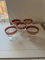 Five vintage coupe glasses arranged on white surface showing red rims with gold stars and wear variation