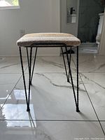 Side view showing black twisted iron legs and square padded seat in striped fabric