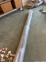 Rolled and unopened area rug on a carpeted floor with furniture nearby.