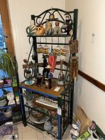 Full view of bakers rack with top and shelves holding decorative bottles, mugs, and various items.