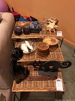 All items arranged on three woven rattan shelves including cat door stops, candles, coasters, glass vase, and starfish shell.