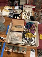 Various jewelry items including necklaces, earrings, watch, bracelets, pendants, ring holders in multiple boxes displayed on table.