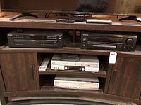 Full view of entertainment unit with Sony CD player, Pioneer stereo receiver on top shelves and JVC and Sylvania VHS/DVD players on middle and bottom shelves.