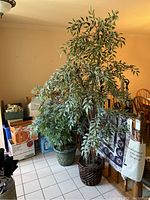 Tall faux tree with variegated green and cream leaves in a woven brown basket-style pot. Visible next to dining area and other items.