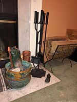 Fireplace tool set with stand alongside a woven basket containing matches and firestarter items, placed on hearth in front of fireplace.