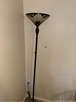Full view of the tall floor lamp showing the dark brown stand and the Tiffany style stained glass shade in a corner.