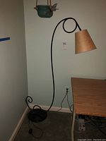 Full view of the vintage floor lamp standing next to a desk and wall outlet. Lamp has black metal stem with an artistic looping curve and beige textured lampshade.