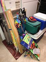 General photo of all items including beach chairs, coolers, sand mats, umbrella, wind spinners, and kite packed together in a basement setting.