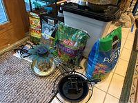 Various bags of potting soil, fertilizer, and bird food arranged with metal yard spinners and bird feeders on floor