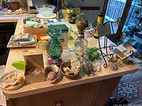 Photo of various items including hummingbird feeder, seashells, coral, glass bottle, figurines, book stand, and small collectibles on a kitchen countertop.