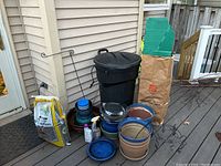 Various garden pots, ceramic planters, terracotta pot, leaf collection helper bag, large bag of sunflower seeds, two spray bottles, metal pot holder, excluding trash can.