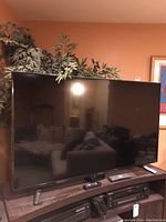 Front view of Sharp 55 inch Roku TV on a wooden stand with remotes, showing screen and legs