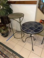 Two side tables shown together; one with a blue ceramic tile top and metal legs, the other with woven metal top and tripod base.