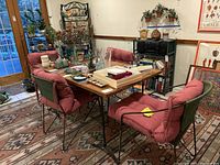 Table and 4 chairs setup in a room with wooden floor and shelf in background showing cushions and table surface.