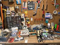 Workbench surface with assorted tools and hardware items spread and boxes of screws and organized hardware