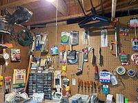 Long view of pegboard wall showing an extensive variety of hand tools, small parts drawers, clamps, brushes, saw blades, drill bits, a wall thermometer, and hanging extension cords.