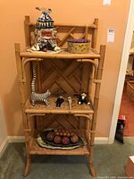 Front view of the three tiered wicker stand with a decorative back, holding some items not included in the lot.