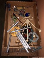 Wind chimes and decorative hanging items in a cardboard box with silver metal tubes, wire decorations, and colorful accents.