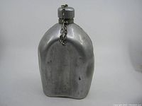 Front view of aluminum US Military canteen with metal screw cap and chain showing dinged surface.