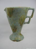 Side view of Art Deco ceramic pitcher showing stepped dual handles, flared spout, and marbled glaze pattern in green, blue, and brown.