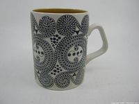 Side view of the mug showing the black hand engraved spiral and dot pattern on white ceramic with the brown interior glaze