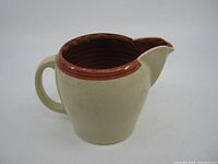 Side view of vintage ceramic creamer showing cream-colored body and brown glazed interior and rim, with handle and pouring spout