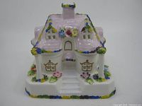 Front view of the porcelain cottage figurine showing the detailed roof with floral decorations and windows.