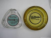 Top view of both ashtrays showing Travel Eze amber round ashtray and clear Motel Doyle triangular ashtray with label.