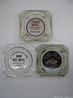 Photo showing three square clear glass ashtrays with printed logos for Shady Rest Motel, Forks Motel, and City Center Motor Hotel from above.