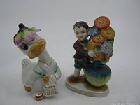Both ceramic figures shown together; Mrs. Duck is white with orange accents and a handbag, boy holds a flower vase.