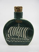 Front view of green ceramic flask with white Viking ship design and cork stopper.