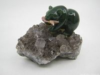 Front angled view showing dark green polished jade bear holding a pink fish on a crystalline rock crystal base with clear and smoky quartz crystals.
