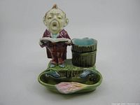 Front view of the majolica matchstick holder depicting a singing man with basin and striker barrel.