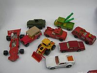 Nine vintage Hot Wheels diecast toy cars displayed in a group, showing a variety of models including military, construction, race, and classic cars, some paint chipped and showing wear.