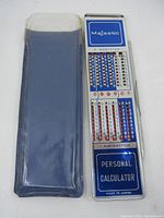 Old metal Majestic personal calculator with protective sleeve shown alongside the calculator unit. Blue sliding cover partially showing.