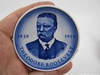 Front view of the ceramic pin dish showing a blue portrait of Theodore Roosevelt along with the years 1858 and 1919 on a white background.