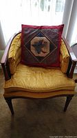 Full view of wood chair with mustard yellow tufted seat and back, cane inserts on back and sides, with wooden arms and legs. Red cushion with horse design on seat.