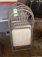 Four metal folding chairs stacked neatly showing the arched back design with metal rods and striped upholstered seats.