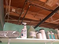 Shelf with ironing board covers and a spray bottle labeled 'Clean Spray', large plastic jug, and several white containers with lids and spray bottles