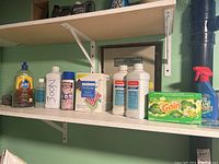 Photo showing shelf with Pledge floor gloss, Silk Wash, large white bottle labeled '300N', two bottles of Kool Wash, Gain fabric softener sheets box, and container of Oxi Clean.