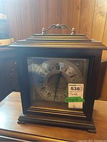 Front angle view of the Bulova wood veneer case clock showing wooden casing, brass handle, and clock face details.