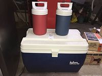 Photo showing one large blue Igloo Legend 48 cooler with white lid and two Playmate water jugs (red and blue) on top.