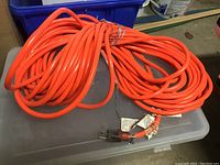 Orange long extension cord coiled on a plastic container showing full length.