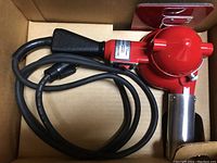 Red Master Heat Gun with black handle and metal heating element housing, showing power cord coiled inside cardboard box.