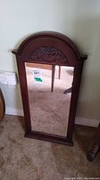 Wall mounted mirror with carved wooden frame, showing front view with a focus on carved details on the top arch.